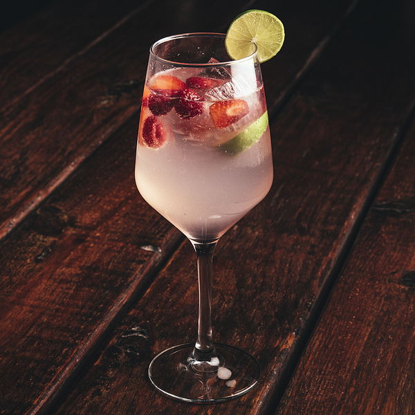 Coctel de la casa con frutos rojos y rodaja de lima en copa de vino